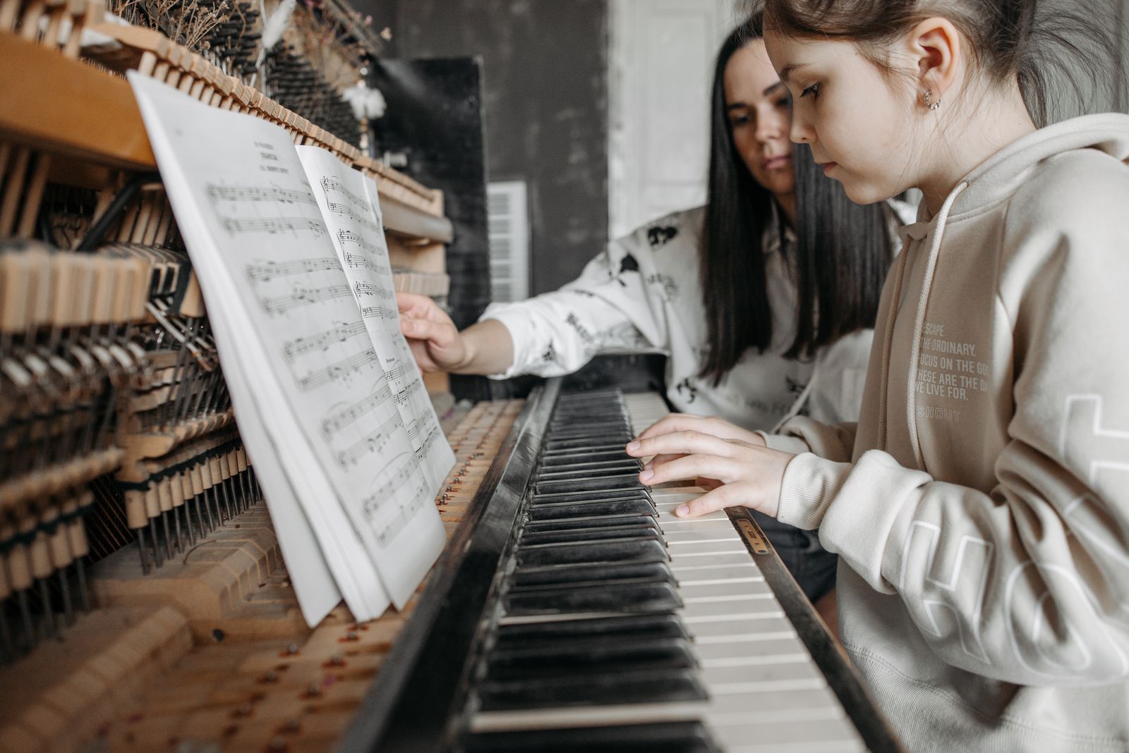 A parent guiding a child through a piano lesson from sheet music at an upright piano