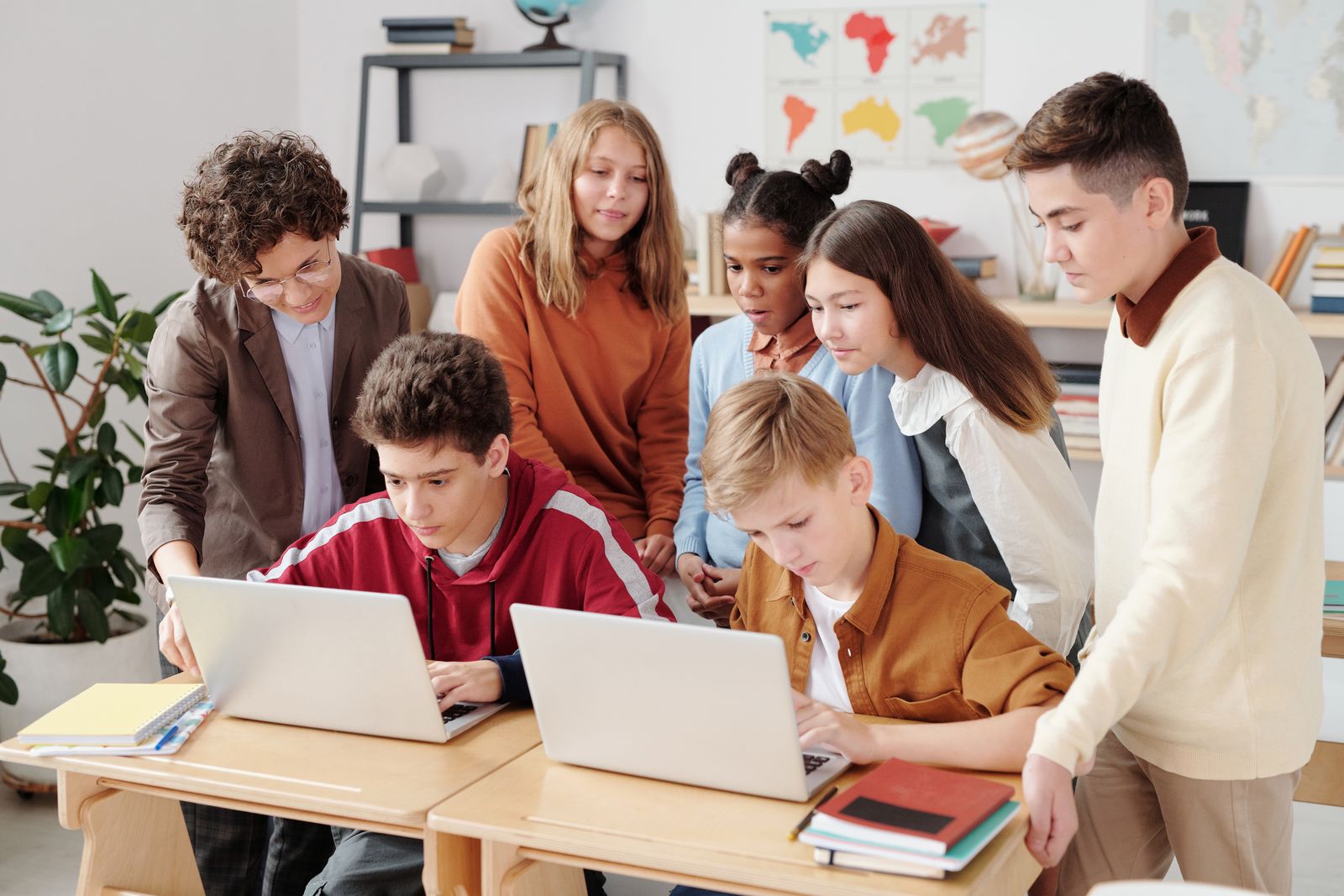 Teacher supervising a group of middle-school students working on laptops in a classroom