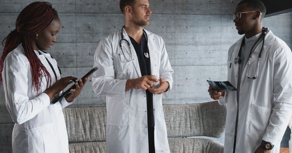 Three healthcare professionals in white coats discussing work in a hospital corridor