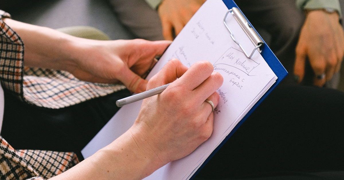A therapist taking notes on a clipboard during a session with a client
