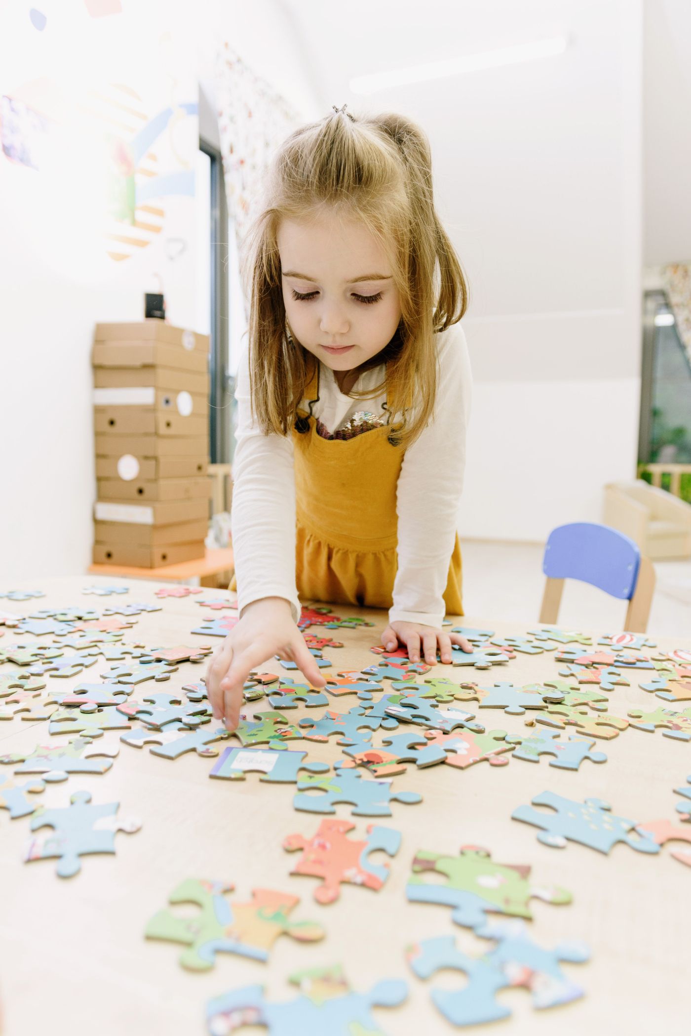 A young girl works methodically through a jigsaw puzzle at a table