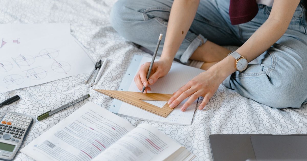 A student studying geometry with a set square, notebook and laptop